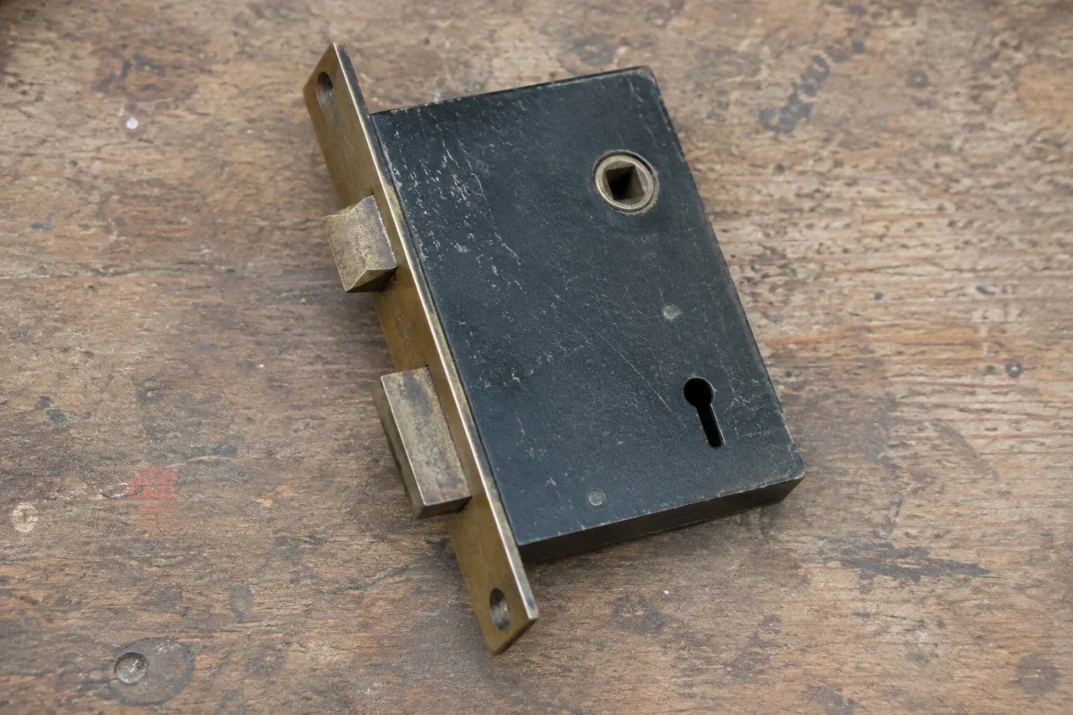 Closed mortise lock case with spindle opening, keyhole, latch and deadbolt on a wooden workbench. — Vintage Mortise Lock Service, Wilmot